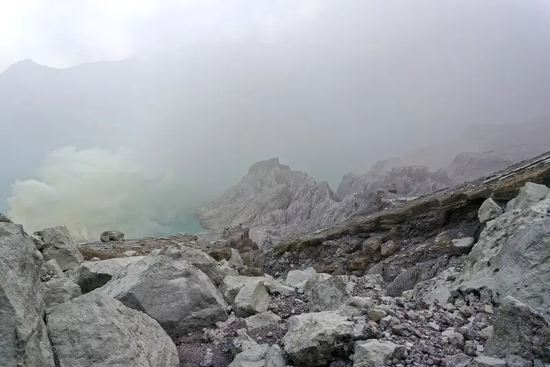 Boulders on the crater floor with sulphur smoke hiding the lake